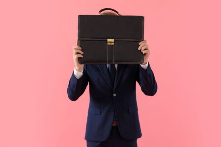 Young businessman covering his face with a briefcase while standing on pink studio backgroundの写真素材