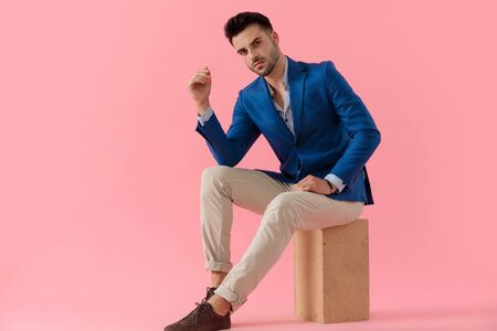 sexy smart casual model holding elbow on knee in a fashion pose on pink background in studio, full bodyの写真素材