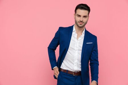 Handsome businessman holding his hand in his pocket while wearing blue suit and standing on pink studio backgroundの写真素材