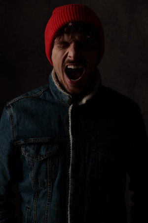 dramatic cool guy wearing red hat and denim jacket, screaming and closing eyes on black background