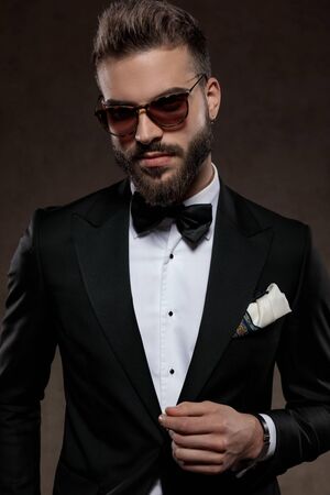 Positive fashion groom smiling while wearing suit and sunglasses, standing on a wallpaper studio backgroundの写真素材