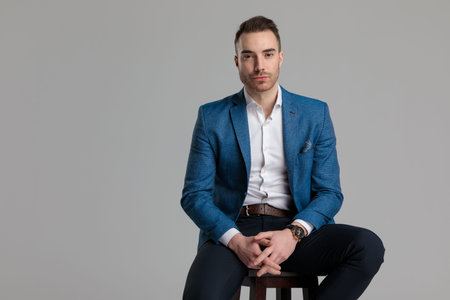 young smartacasual model crossing fingers and sitting on wooden chair on grey backgroundの写真素材