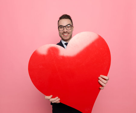 upset young man in suit holding fist up, pointing finger and threatening, standing on pink backgroundの写真素材