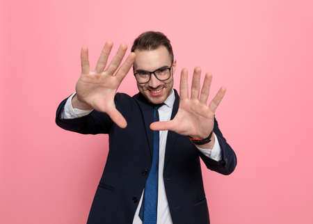 smiling young businessman in suit wearing glasses and framing, standing on pink backgroundの写真素材
