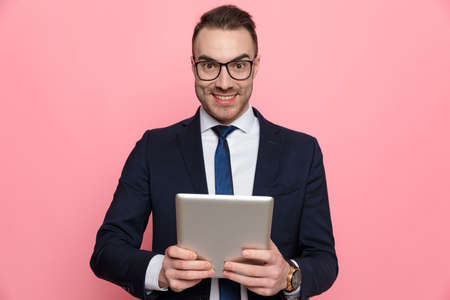 happy elegant businessman in suit wearing glasses, holding blackboard and smiling, standing on pink backgroundの写真素材