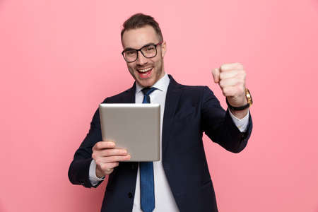 happy elegant businessman in suit wearing glasses, holding blackboard and smiling, standing on pink backgroundの写真素材