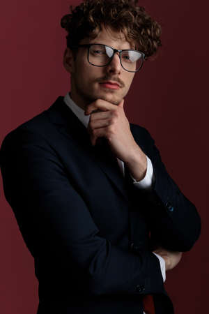 elegant fashion businessman with sensual attitude touching his chin and looking at the camera on pink studio backgroundの写真素材