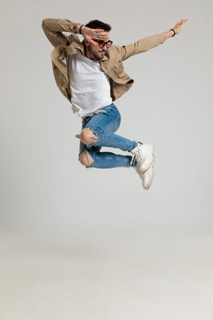 sexy young casual guy in jacket wearing sunglasses, holding hands in the air, looking to side and...