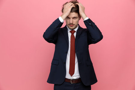 elegant young businessman in navy blue suit running fingers through hair and arranging it, standing...