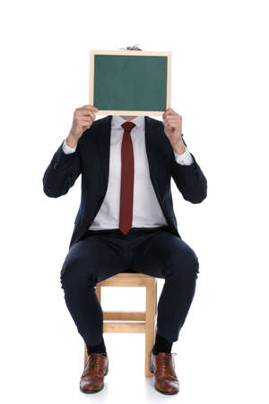 businessman hiding his face behind a board, sitting against white backgroundの写真素材