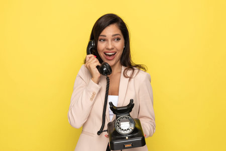 enthusiastic young girl in pink suit talking on the old rotary telephone, laughing and looking to...