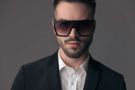 Closeup of confident fashion model wearing suit and sunglasses while standing on gray studio backgroundの写真素材