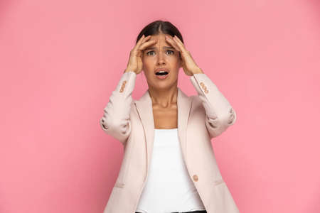 beautiful smart casual woman is looking at the camera and feeling shocked, slapping her head against pink backgroundの写真素材