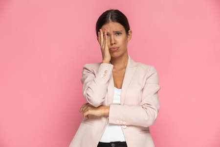 attractive businesswoman feeling overwhelmed, slapping her face and puffing her cheeks against pink backgroundの写真素材