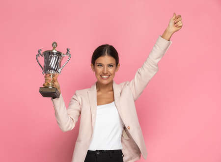 cute businesswoman holding a cup and giving a thumbs up in the air against pink backgroundの写真素材
