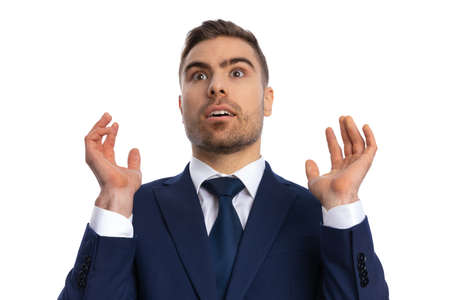 surprised unshaved man in navy blue suit looking up and shockingly hand gesturing on white background in studioの写真素材