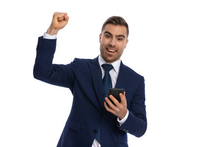 enthusiastic businessman in navy blue suit holding fists in the air and celebrating victory while...
