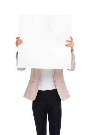 young woman in pink jacket hiding behind white empty board, standing and posing isolated on white background in studioの写真素材