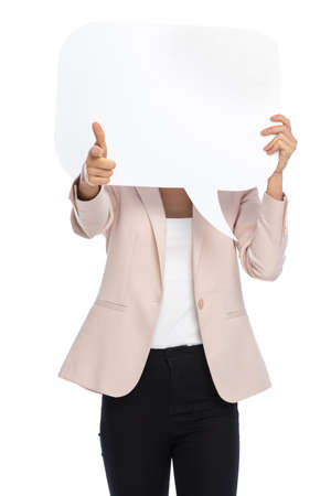 young businesswoman in pink jacket hiding behind empty speech bubble on white background, pointing fingers and posing in studioの写真素材