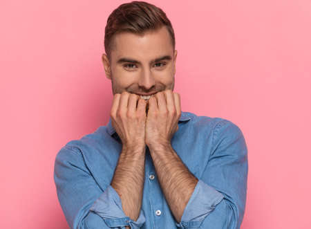 portrait of excited casual man in denim shirt holding finger to mouth and enthusiastically waiting and smiling on pink background in studioの写真素材