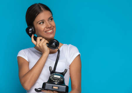 beautiful casual woman smiling while talking on her vintage telephone against blue backgroundの写真素材