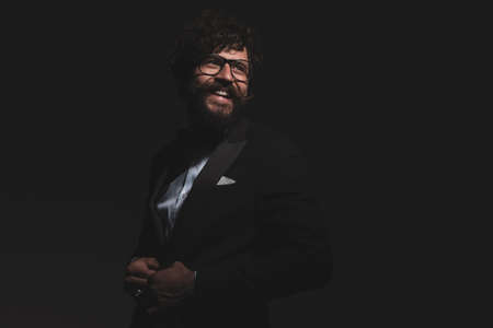 young handsome businessman closing his tuxedo, smiling and having a good time, wearing eyeglasses on gray backgroundの写真素材