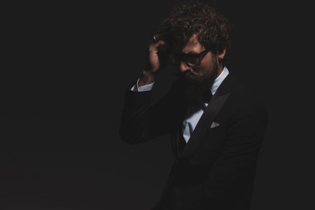 sexy businessman fixing his hair, wearing glasses and tuxedo, looking down and being dramatic