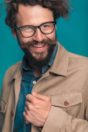 happy casual young man with glasses holding jacket, arranging and smiling on blue background in studio, portraitの写真素材
