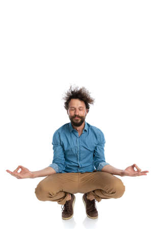 young casual man squatting and meditating, making yoga exercises on white backgroundの写真素材