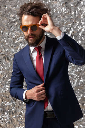 sexy businessman adjusting his sunglasses and closing his jacket with style on staniol backgroundの写真素材