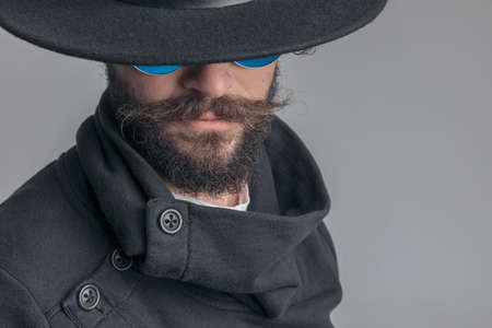 close up on a mysterious casual man wearing sunglasses and hiding his face under a hat on gray backgroundの写真素材