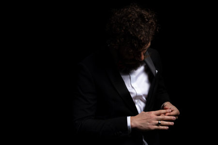 young businessman rubbing his palms and looking down, being dramatic on black studio background
