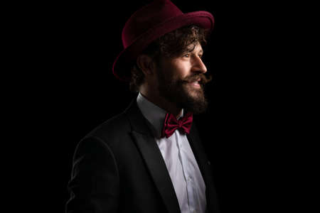 side view of a happy businessman looking away and smiling, wearing a burgundy hat against black backgroundの写真素材