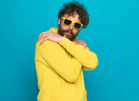 cool casual guy with long beard and moustache hugging and protecting himself in front of blue background in studioの写真素材