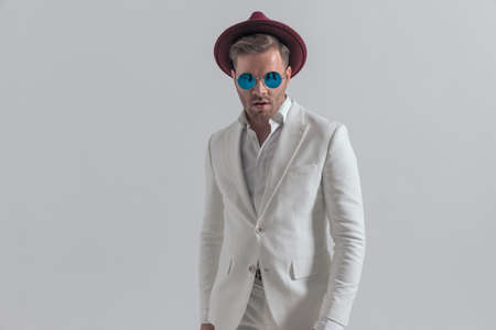 sexy young businessman wearing a burgundy hat and sunglasses, posing against gray backgroundの写真素材