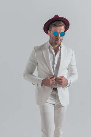 cool fashion model fixing his jacket, wearing a hat and sunglasses against gray backgroundの写真素材