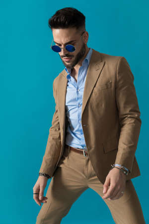 bearded businessman with glasses looking down and posing in a fashion manner on blue background in studioの写真素材