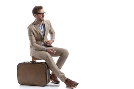 sexy businessman sitting on a chair, next to his briefcase, fixing his suit and wearing eyeglassesの写真素材