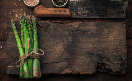 top view of a fresh asparagus bunch on very old wood chopping board with copy space for your mesagge, near salt and pepper bowls and vintae cleaverの写真素材