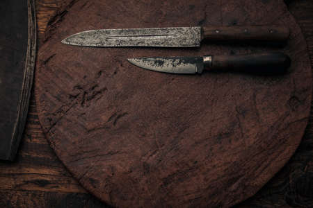 two vintage knives on an old wooden round cutting board near a cleaver blade , top view with copy spaceの写真素材