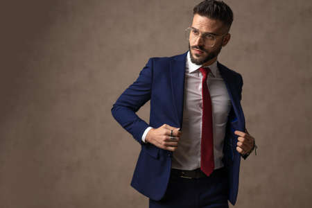 handsome businessman opening his suit, wearing eyeglasses and posing against wallpaperの写真素材