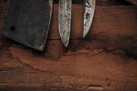 closeup of the tips of knives and a cleaver on an old wooden cutting boardの写真素材
