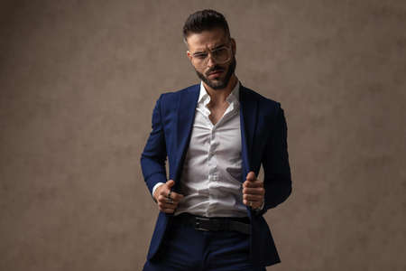 sexy fashion model pulling his jacket, looking away and wearing eyeglasses with attitudeの写真素材