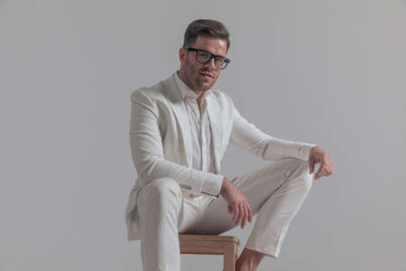 sexy businessman posing on a chair, feeling relaxed and smiling at the camera on white backgroundの写真素材