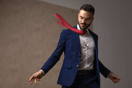 young businessman posing with his tie in the air, looking down and wearing eyeglassesの写真素材