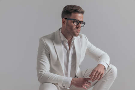 seated handsome businessman looking to side, wearing eyeglasses and posing against white backgroundの写真素材
