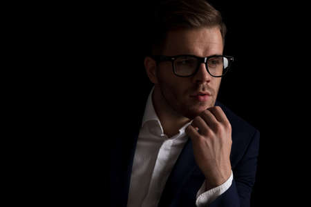 portrait of attractive businessman with glasses looking to side and thinking while posing in a fashion light on black background in studioの写真素材