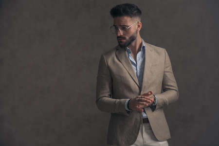 sexy unshaved businessman with glasses rubbing palms and looking to side on brown background in studioの写真素材