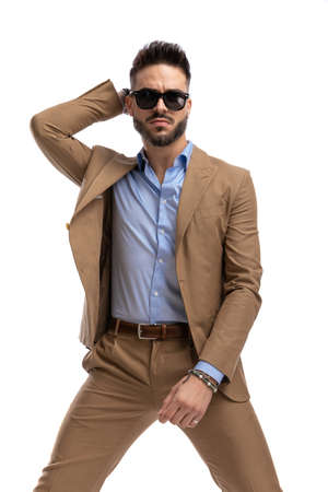 confident bearded man with glasses holding hand behind head and posing in a fashion manner on white background in studioの写真素材