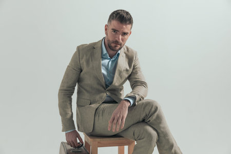 man in suit with luggage sitting on wooden chair and taking some days off to go on holiday, posing...